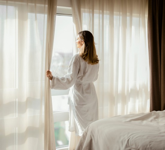 a woman in a white robe opening curtains