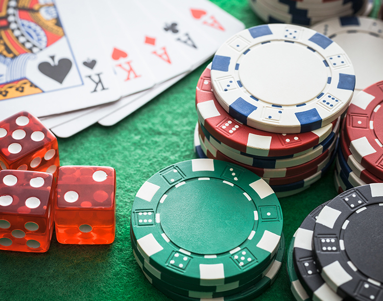 Close-up of casino chips (red, green, blue), two clear red dice, and playing cards (Kings and Aces) on a green felt surface.