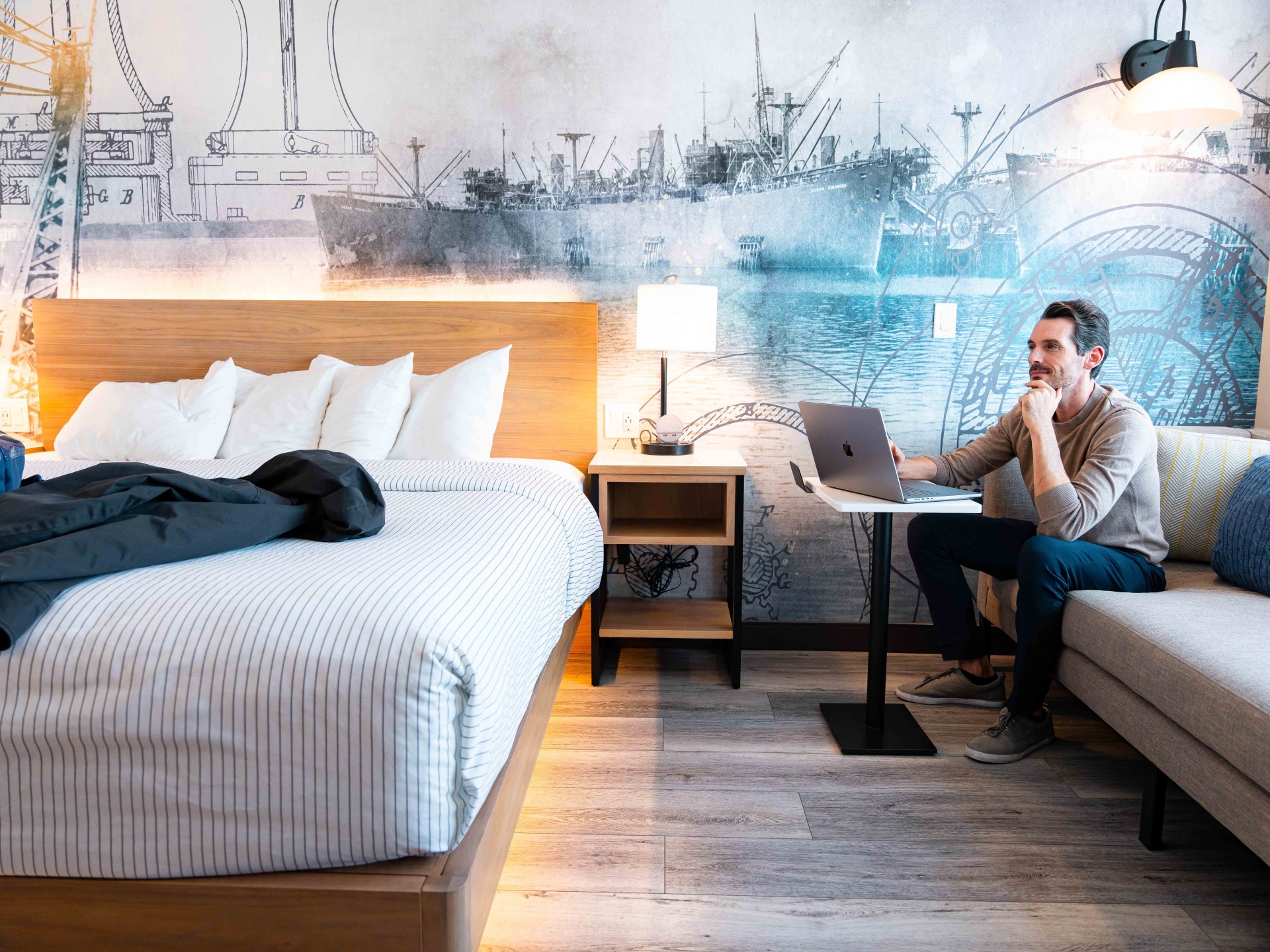 a man sitting on a couch with a laptop in front of a bed