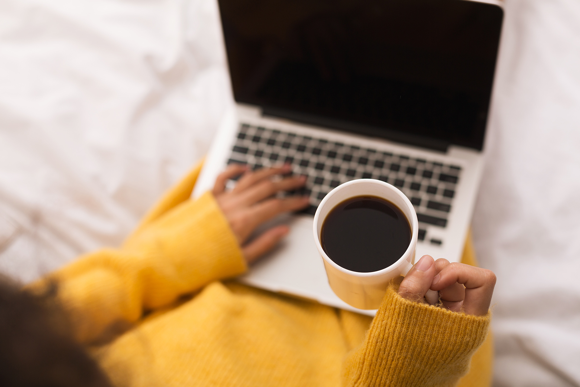 person on laptop and holding a mug of coffee