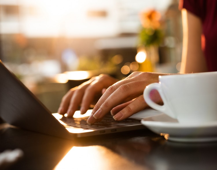 person typing on their laptop with a coffee cup next to them