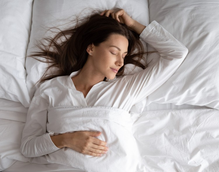 woman sleeping in bed with one hand on stomach and the other above her head