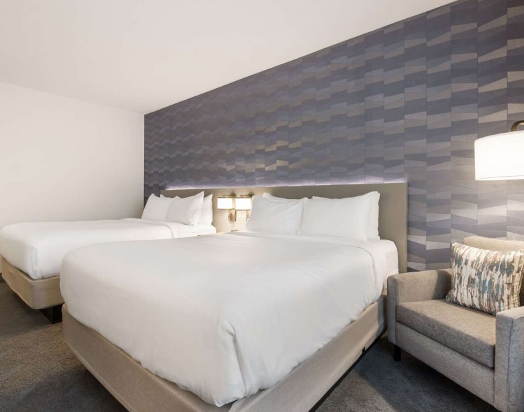 2 queen beds with gray chair next to bed