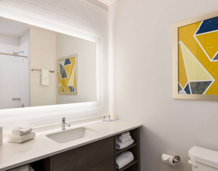 bathroom with white illuminated mirror and yellow and blue painting on wall