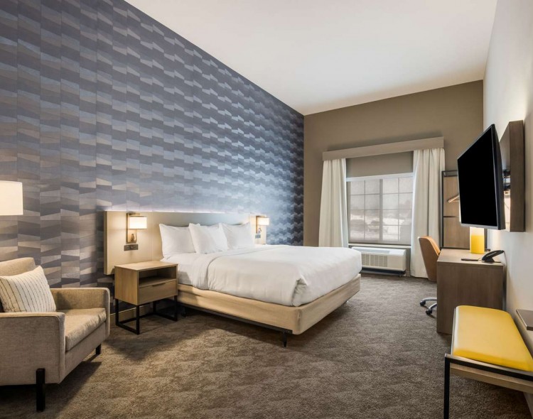 king bed with mounted tv across from it and gray chair next to bed