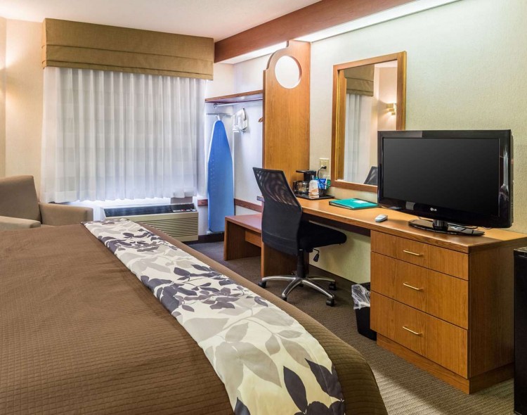 end of bed with flowered bedrunner and chair next to bed with hanging space and tv on desk