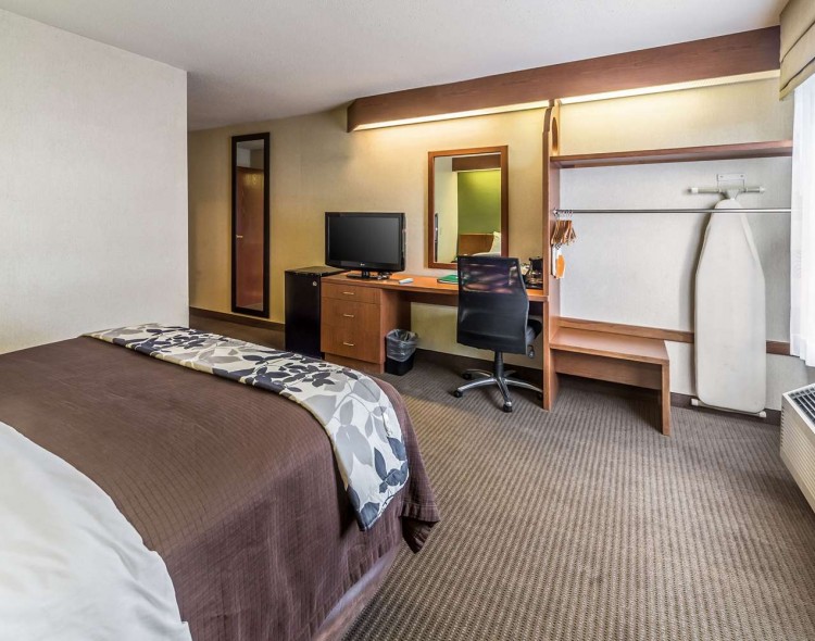 bed with ironing board, hanging space, desk, and mirror across from bed