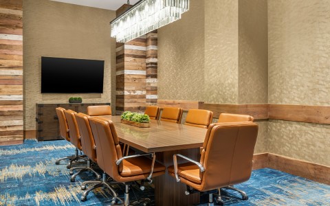 A contemporary boardroom featuring a long wooden conference table surrounded by ten tan leather chairs.