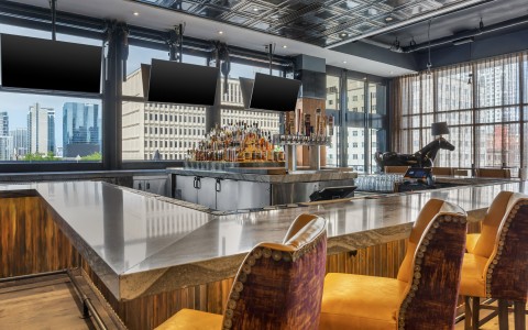 A modern indoor bar featuring a long, polished marble countertop with modern yellow and purple cushioned barstools.