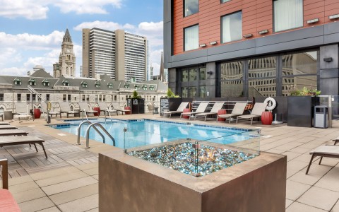 An outdoor rooftop swimming pool surrounded by a tan tiled deck with modern lounge chairs.