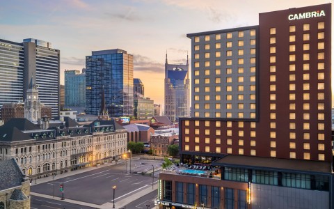 An elevated twilight view of the Cambria hotel building, its windows warmly lit against a sunset sky.