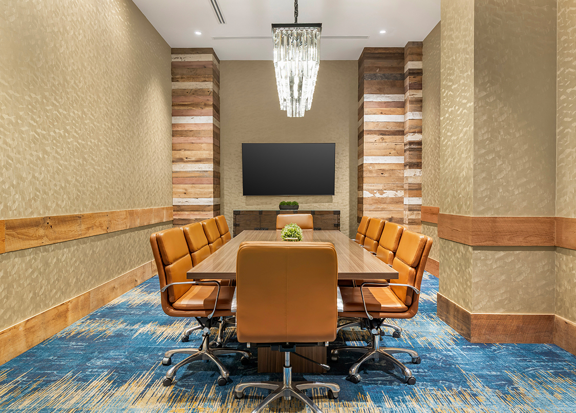 A contemporary boardroom featuring a long wooden conference table surrounded by ten tan leather chairs.