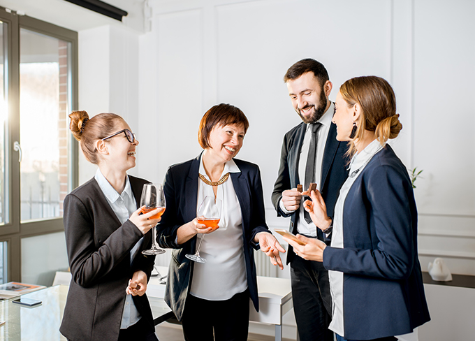 Well dressed three women and a guy gathered having a drink and smiling looking at each other