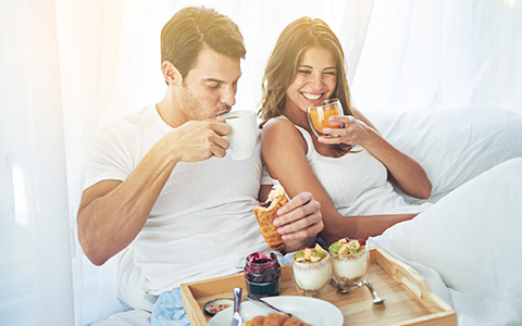 A couple is eating breakfast in bed,