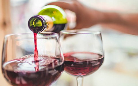 close up of person pouring red wine into glasses