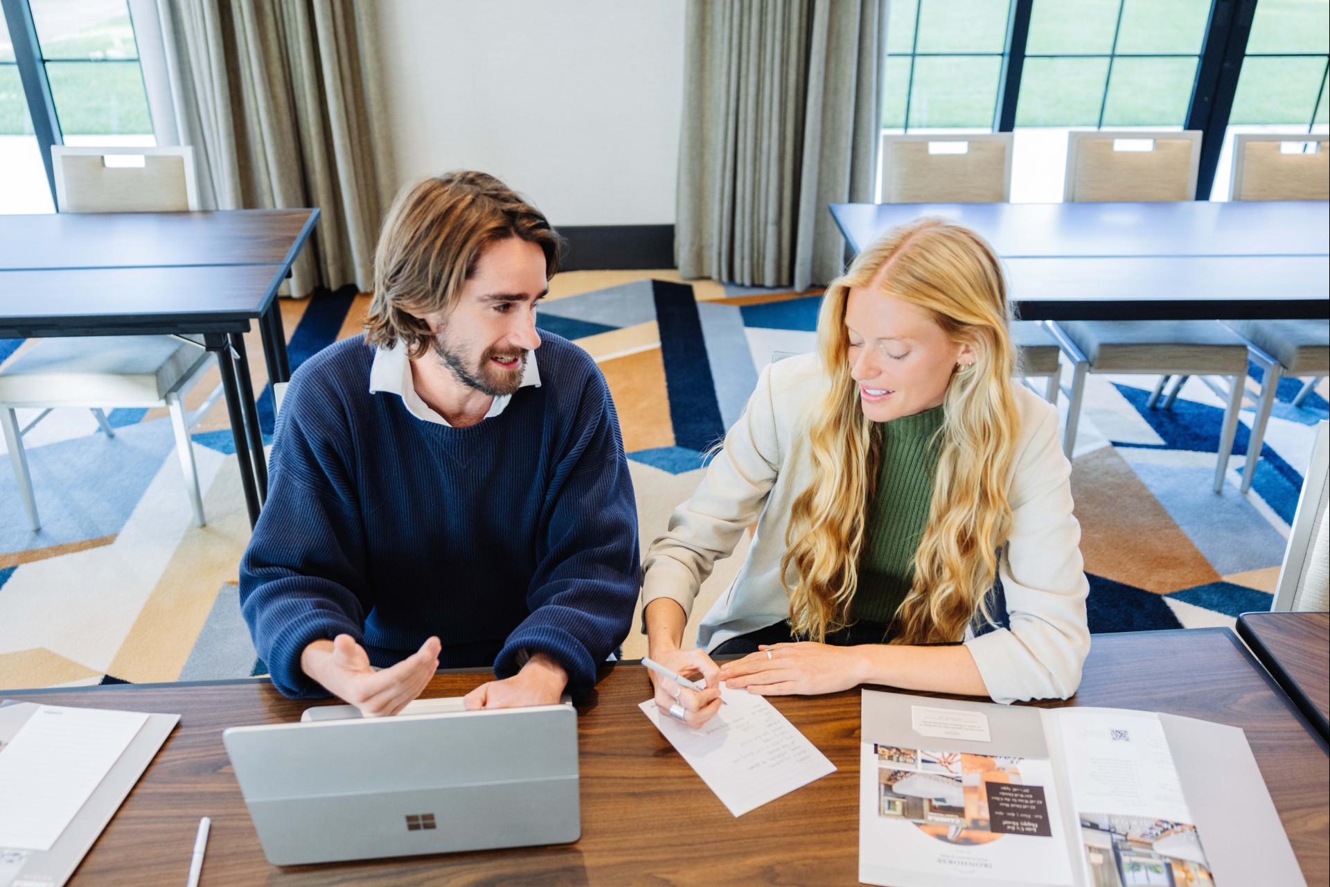 a man and woman sitting at a table with papers and a laptop