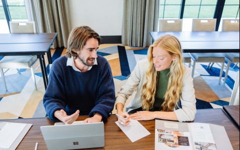 a man and woman sitting at a table with papers and a laptop