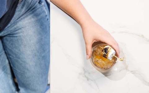 a person holding a drink with a marshmallow on a stick