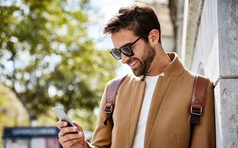 a man wearing sunglasses and a brown jacket looking at a cellphone