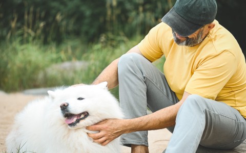 a man sitting on a rock petting a white dog